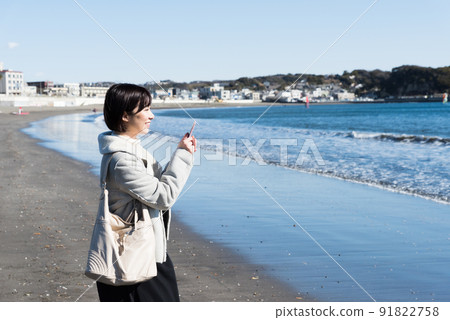A woman taking a picture of the winter coast with a smartphone 91822758