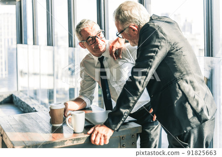 Picture of two business men negotiating over a deal. One man is in his 70th he is wearing black suit. The other man is in his 40th he is wearing a white shirt and black tie. They sat in lounge. Picture of two business men negotiating over a deal. One man is in his 70th he is wearing black suit. The other man is in his 40th he is wearing a white shirt and black tie. They sat in lounge. 91825663