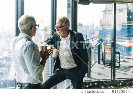 Picture of two business men negotiating over a deal. One man is in his 70th he is wearing black suit. The other man is in his 40th he is wearing a white shirt and black tie. They sat in lounge. Picture of two business men negotiating over a deal. One man is in his 70th he is wearing black suit. The other man is in his 40th he is wearing a white shirt and black tie. They sat in lounge. 91825664