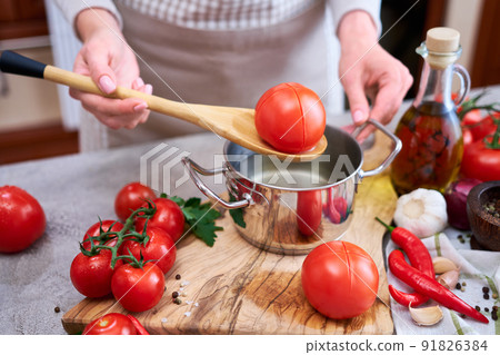 woman blanching a tomato holding over pan with hot water for further peeling woman blanching a tomato holding over pan with hot water for further peeling 91826384