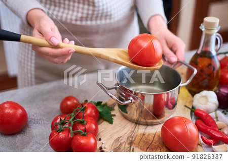 woman blanching a tomato holding over pan with hot water for further peeling woman blanching a tomato holding over pan with hot water for further peeling 91826387