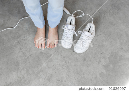 Woman stands barefoot near white shoes drying with electric dryer 91826997