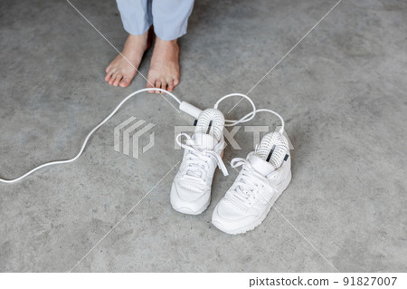 Woman stands barefoot near white shoes drying with electric dryer Woman stands barefoot near white shoes drying with electric dryer 91827007