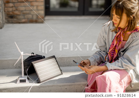 Woman charge phone from a portable solar panel Woman charge phone from a portable solar panel 91828614