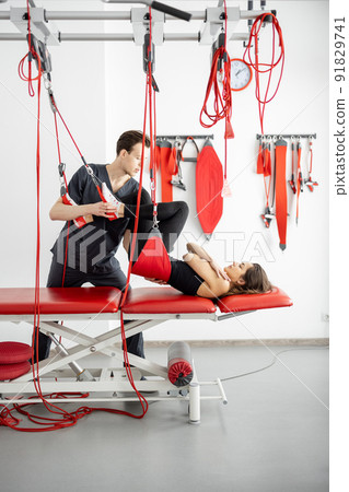 Rehabilitation specialist doing active treatment on suspension straps to a male patient Rehabilitation specialist doing active treatment on suspension straps to a male patient 91829741
