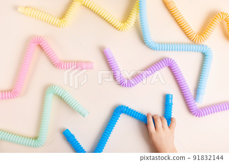 Trendy kids toys pastel colorful pop-tube in baby toddler hands on beige background. Set of forms and colors corrugated pipe and anti stressing, relaxation fidget finger toys. Trendy kids toys pastel colorful pop-tube in baby toddler hands on beige background. Set of forms and colors corrugated pipe and anti stressing, relaxation fidget finger toys. 91832144