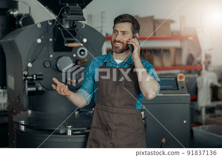 Business owner of coffee factory talking phone on background of coffee roasting machine 91837136