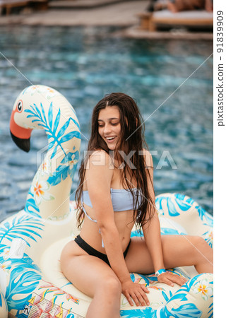 Woman on inflatable Flamingo floating in swimming pool. 91839909