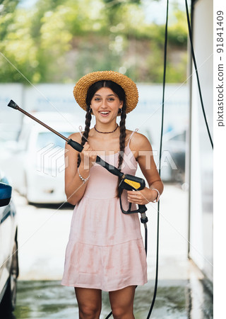 Woman with high pressure hose at car wash Woman with high pressure hose at car wash 91841409