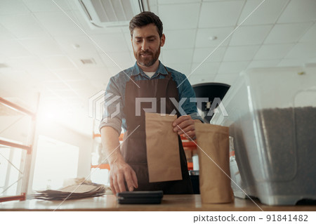 Uniformed worker packs roasted coffee beans into packages for sale 91841482