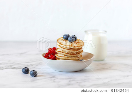 Homemade mini pancakes served with blueberries and red currants and joghurt 91842464