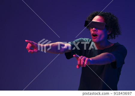 Shocked confused stylish tanned curly man in black t-shirt trendy eyewear posing isolated on color pink blue background. Cool fashion offer. Virtual Reality New Collection concept. Copy space for ad 91843697