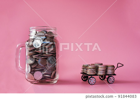 coins in classic glass jar and coins in cart on pink background saving and investment concept coins in classic glass jar and coins in cart on pink background saving and investment concept 91844083