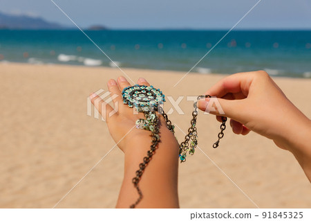Female hands with many boho bracelets, and sand in the beach. Female hands with many boho bracelets, and sand in the beach. 91845325