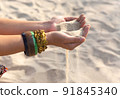Female hands with many boho bracelets, and sand in the beach. 91845340