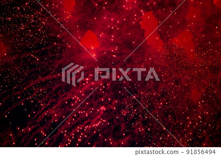 A bright firework with a red glowing center with red sparks and smoke flying towards the background of the night sky. High quality photo 91856494