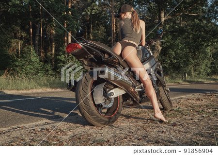 Young sexy woman biker in bikini sitting on a motorcycle on the side of a forest road Young sexy woman biker in bikini sitting on a motorcycle on the side of a forest road 91856904