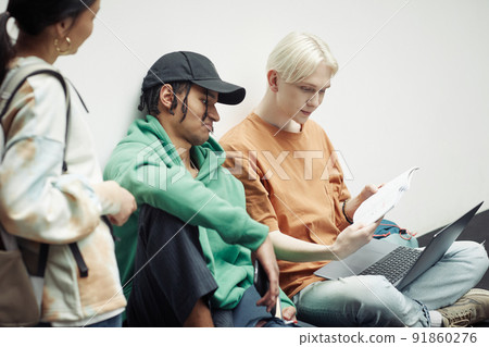 Two intercultural teenage guys looking through lecture notes in copybook Two intercultural teenage guys looking through lecture notes in copybook 91860276
