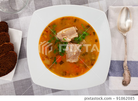 Pickle soup with pearl barley, potatoes, onions, carrots and parsley. Rassolnik in a white plate on a marble background. Traditional dish of Russian cuisine 91862085