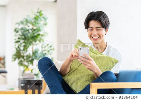A young man looking at his smartphone in the living room A young man looking at his smartphone in the living room 91864104
