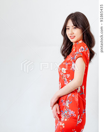 Beautiful young Asian woman in traditional cheongsam standing in front of white background Beautiful young Asian woman in traditional cheongsam standing in front of white background 91865435