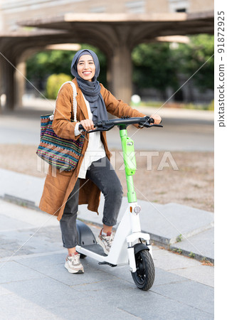 Muslim woman using an electric scooter in the street 91872925