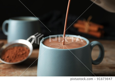 Pouring hot cocoa drink into cup on wooden table Pouring hot cocoa drink into cup on wooden table 91873647