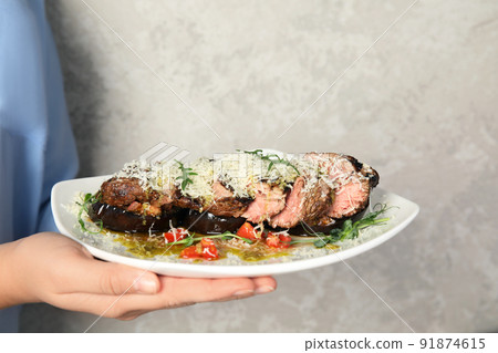 Woman holding plate with delicious roasted meat on grey background, closeup 91874615