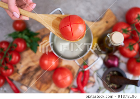 woman blanching a tomato holding over pan with hot water for further peeling woman blanching a tomato holding over pan with hot water for further peeling 91878196