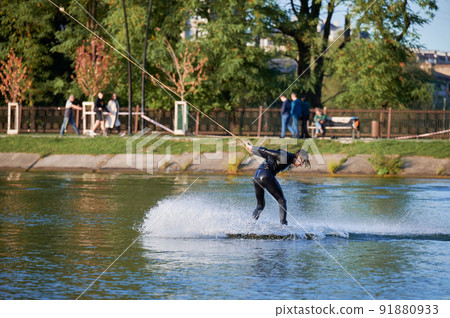 Wakeboarder making tricks while wakeboarding on lake. Young man surfer having fun wakesurfing in the cable park. Water sport, outdoor activity concept. 91880933