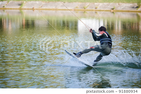 Wakeboarder surfing on lake. Young man surfer having fun wakeboarding in the cable park. Water sport, outdoor activity concept. 91880934