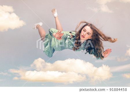 Beautiful girl levitating in mid-air, falling down and her hair messed up soaring from wind, model flying hovering with dreamy peaceful expression in sky. collage composition on day cloudy blue sky Beautiful girl levitating in mid-air, falling down and her hair messed up soaring from wind, model flying hovering with dreamy peaceful expression in sky. collage composition on day cloudy blue sky 91884458