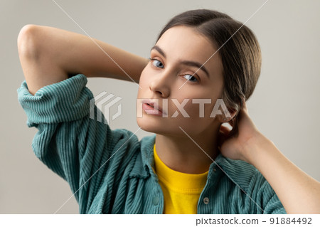 Closeup portrait of beautiful dark haired woman looking at camera, having romantic expression, posing with raised arms, wearing casual style jacket. Indoor studio shot isolated on gray background. Closeup portrait of beautiful dark haired woman looking at camera, having romantic expression, posing with raised arms, wearing casual style jacket. Indoor studio shot isolated on gray background. 91884492