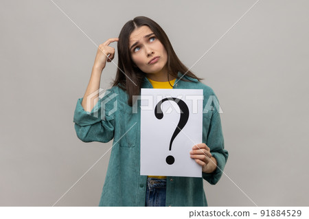 Portrait of pensive thoughtful woman looking away, holding paper with question mark, thinks about solving problem, wearing casual style jacket. Indoor studio shot isolated on gray background. Portrait of pensive thoughtful woman looking away, holding paper with question mark, thinks about solving problem, wearing casual style jacket. Indoor studio shot isolated on gray background. 91884529