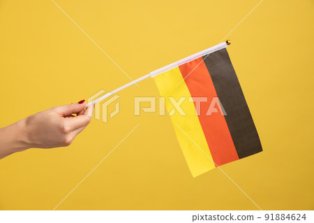 Profile side view closeup of woman hand holding Germany flag. Day of Germany - 3th October. Indoor studio shot isolated on yellow background. Profile side view closeup of woman hand holding Germany flag. Day of Germany - 3th October. Indoor studio shot isolated on yellow background. 91884624