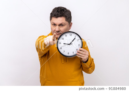 Portrait of happy positive man holding big wall clock and pointing to camera with pleasant smile, time to go, wearing urban style hoodie. Indoor studio shot isolated on white background. 91884980