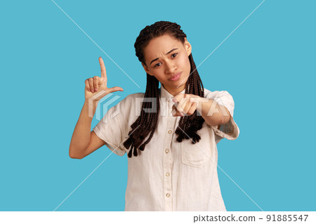 You are loser. Portrait of bossy serious woman with dreadlocks showing loser gesture and pointing at camera, accusing for failure, wearing white shirt. Indoor studio shot isolated on blue background. You are loser. Portrait of bossy serious woman with dreadlocks showing loser gesture and pointing at camera, accusing for failure, wearing white shirt. Indoor studio shot isolated on blue background. 91885547