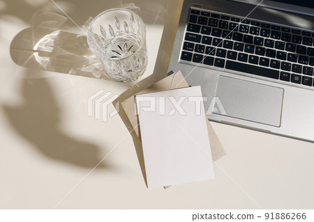Summer workspace composition with open laptop. Greeting card, invitation mockup. Glass of water, fresh drink in sunlight. Long shadows overlay. Beige table background. Business concept. Flat lay, top 91886266