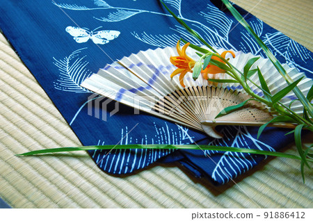 Blue yukata, folding fan and summer flowers on tatami mats. Blue yukata, folding fan and summer flowers on tatami mats. 91886412