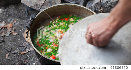Freshly cooked hot soup in old cauldron on camp fire and man hand with pot cover 91886550