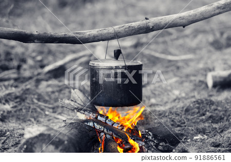 Cooking in sooty cauldron on campfire at forest. Black and white selective color effect. Cooking in sooty cauldron on campfire at forest. Black and white selective color effect. 91886561