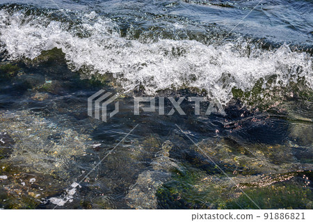 Sea waves crash against large rocks on the shore, forming large splashes Sea waves crash against large rocks on the shore, forming large splashes 91886821