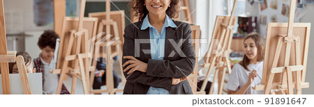Portrait of smiling female arfican american teacher in modern classroom with kids drawing lesson in background 91891647
