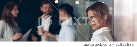 Mature smiling business lady at office with group of colleagues on background, working on laptop 91891656