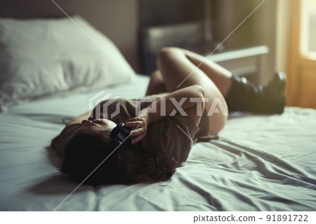 Beautiful young naked woman in headphones listening music lying on a bed in the bedroom near window at sunset. Beautiful young naked woman in headphones listening music lying on a bed in the bedroom near window at sunset. 91891722