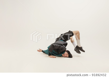 Stylish young man in black outfit and green coat posing, lying on floor isolated over grey studio background. Flexibility. Stylish young man in black outfit and green coat posing, lying on floor isolated over grey studio background. Flexibility. 91892432