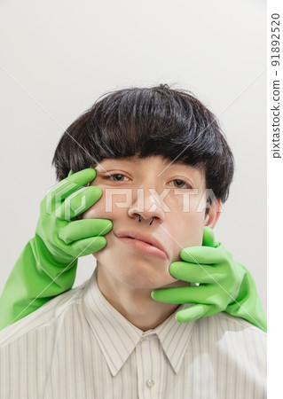 Portrait of young man with piercing posing with hands in rubber gloves on face isolated over grey studio background 91892520