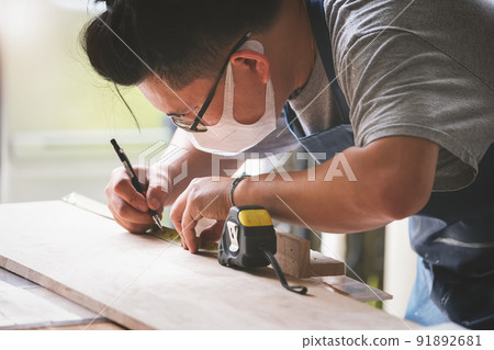 A carpenter measures the planks to assemble the parts and build a wooden table for the customer 91892681