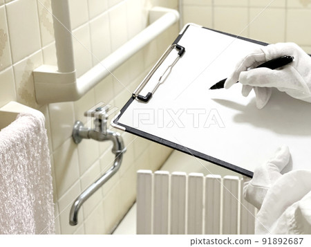 Hands of white gloves with a clipboard to assess the handrail of the bath Hands of white gloves with a clipboard to assess the handrail of the bath 91892687