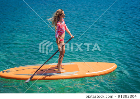 Young women Having Fun Stand Up Paddling in blue water sea in Montenegro. SUP. girl Training on Paddle Board near the rocks Young women Having Fun Stand Up Paddling in blue water sea in Montenegro. SUP. girl Training on Paddle Board near the rocks 91892804
